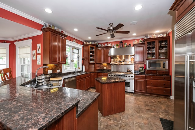 kitchen featuring ceiling fan, sink, wall chimney exhaust hood, built in appliances, and a center island