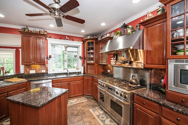 kitchen featuring ceiling fan, sink, wall chimney range hood, appliances with stainless steel finishes, and decorative backsplash