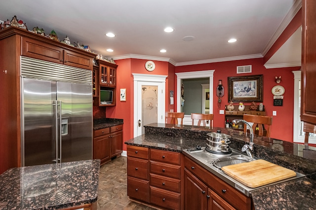 kitchen featuring dark stone counters, crown molding, stainless steel built in refrigerator, and sink