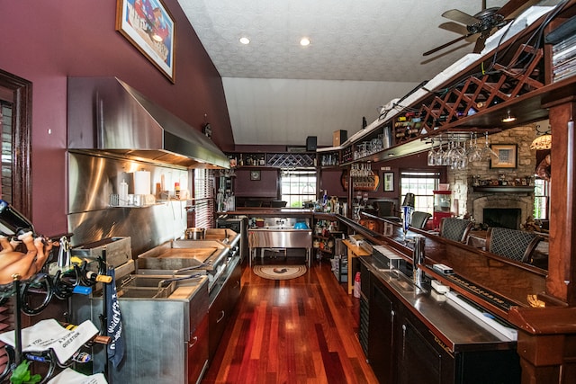 kitchen featuring a textured ceiling, dark wood-type flooring, lofted ceiling, a stone fireplace, and ceiling fan