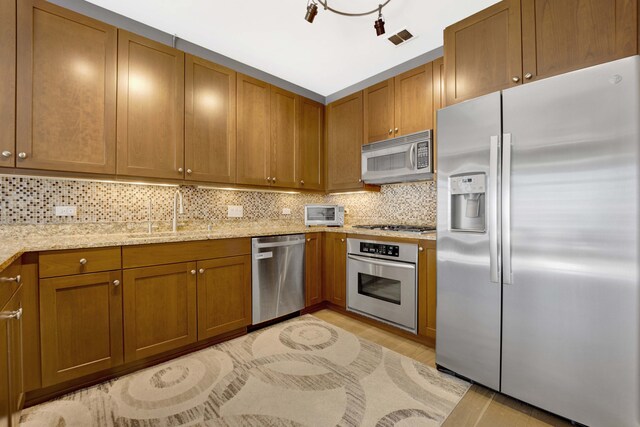 kitchen featuring light stone counters, sink, decorative backsplash, stainless steel appliances, and light hardwood / wood-style flooring