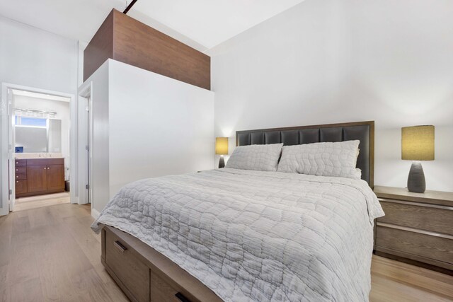 bedroom featuring light hardwood / wood-style flooring, a towering ceiling, and ensuite bath