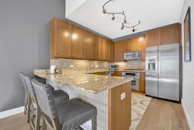 kitchen with kitchen peninsula, tasteful backsplash, stainless steel appliances, light stone countertops, and light hardwood / wood-style floors