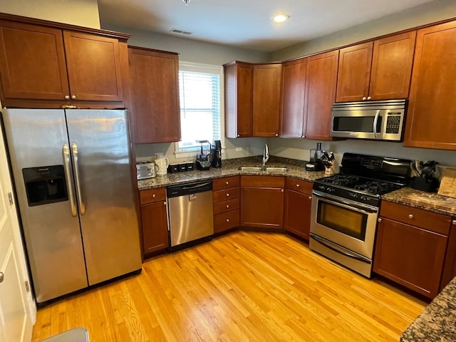 kitchen with stainless steel appliances, dark stone countertops, light hardwood / wood-style floors, and sink