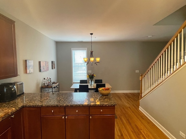 kitchen featuring dark stone countertops, kitchen peninsula, pendant lighting, an inviting chandelier, and light hardwood / wood-style flooring