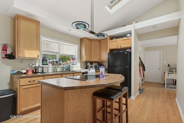 kitchen featuring a kitchen island, black appliances, lofted ceiling with skylight, light brown cabinetry, and light hardwood / wood-style flooring