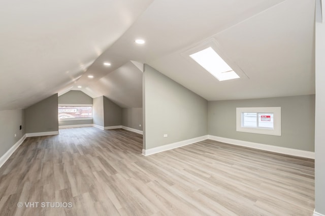 additional living space with vaulted ceiling with skylight and light hardwood / wood-style flooring