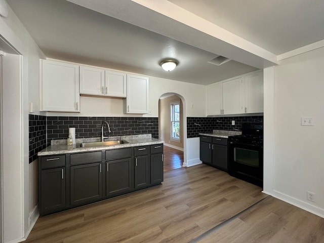 kitchen with white cabinets, backsplash, hardwood / wood-style flooring, black electric range oven, and sink