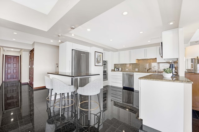 kitchen featuring white cabinets, tasteful backsplash, stone countertops, stainless steel appliances, and a tray ceiling