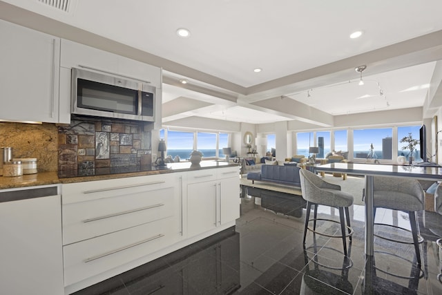 kitchen featuring dark stone counters, white cabinets, beam ceiling, decorative backsplash, and a water view