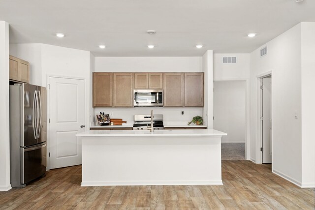 kitchen with light hardwood / wood-style floors, a kitchen island with sink, sink, and stainless steel appliances