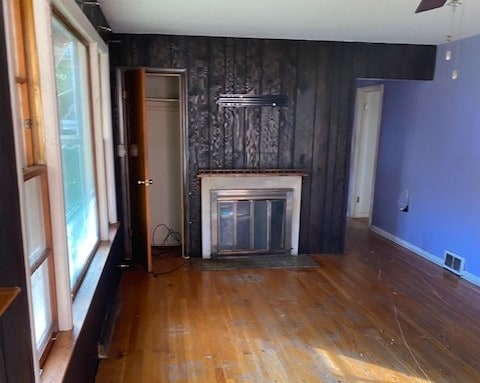 unfurnished living room featuring wood walls, ceiling fan, a healthy amount of sunlight, and wood-type flooring