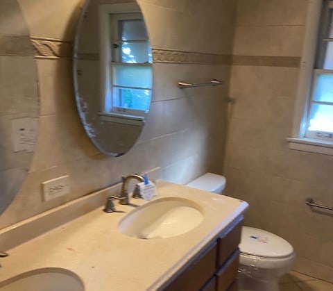 bathroom with vanity, toilet, and tile walls