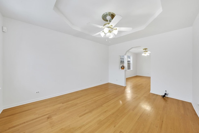 unfurnished living room with light hardwood / wood-style flooring, ceiling fan, and a tray ceiling