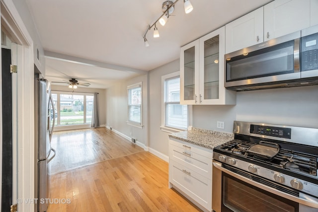 kitchen featuring white cabinets, light hardwood / wood-style flooring, stainless steel appliances, light stone countertops, and ceiling fan