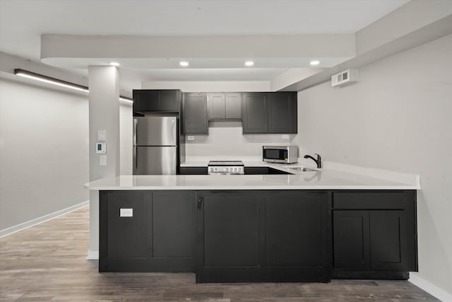 kitchen with kitchen peninsula, appliances with stainless steel finishes, and hardwood / wood-style flooring