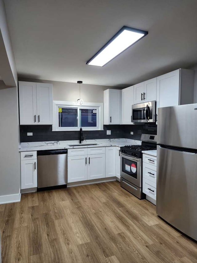 kitchen with hanging light fixtures, white cabinetry, light hardwood / wood-style flooring, and stainless steel appliances