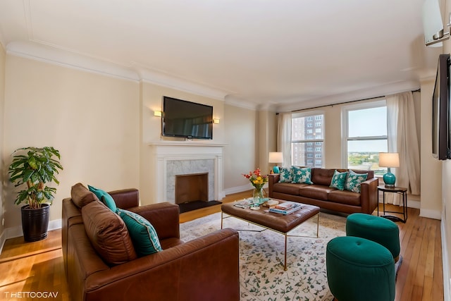 living room featuring a high end fireplace, ornamental molding, and light wood-type flooring