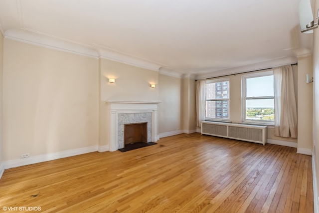 unfurnished living room with crown molding, radiator heating unit, a high end fireplace, and light wood-type flooring