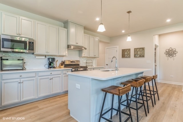 kitchen with stainless steel appliances, pendant lighting, an island with sink, and light hardwood / wood-style flooring