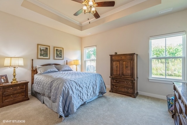 carpeted bedroom with ceiling fan, ornamental molding, a tray ceiling, and multiple windows