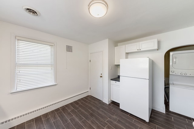 kitchen with white cabinets, white refrigerator, stacked washing maching and dryer, dark hardwood / wood-style floors, and a baseboard radiator