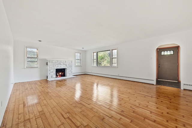 unfurnished living room with a stone fireplace, a baseboard radiator, light wood-type flooring, and plenty of natural light