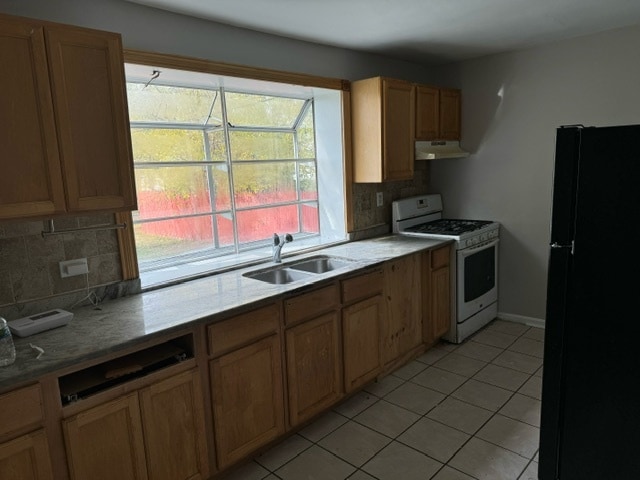 kitchen featuring tasteful backsplash, light tile patterned floors, black fridge, sink, and white gas range oven