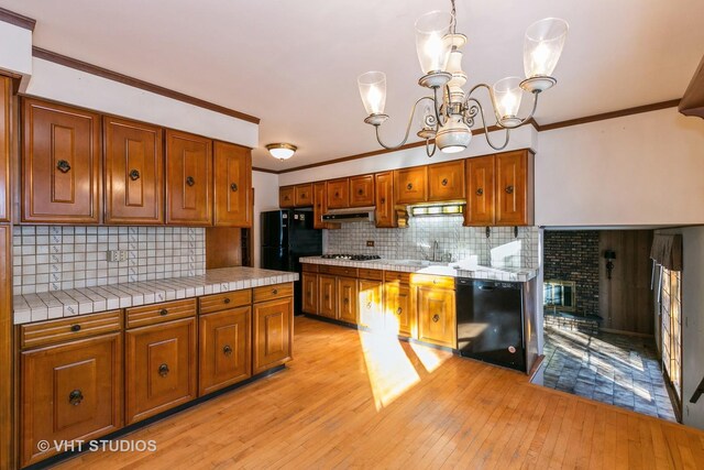 kitchen featuring light hardwood / wood-style floors, ventilation hood, a chandelier, pendant lighting, and black appliances