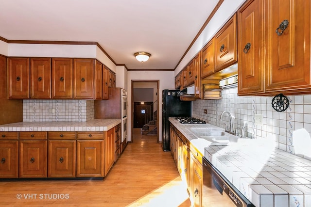 kitchen with dishwasher, tasteful backsplash, light hardwood / wood-style floors, sink, and tile countertops