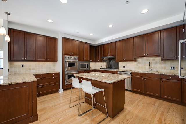 kitchen featuring sink, decorative light fixtures, appliances with stainless steel finishes, light wood-type flooring, and a kitchen bar