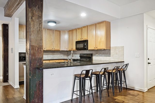 kitchen featuring black appliances, kitchen peninsula, dark wood-type flooring, and tasteful backsplash