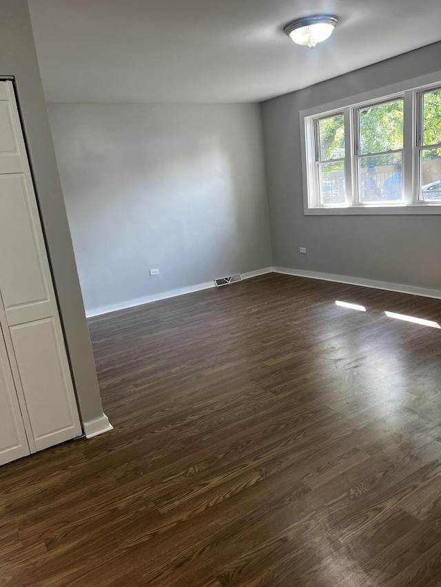 empty room featuring dark wood-type flooring, baseboards, and visible vents