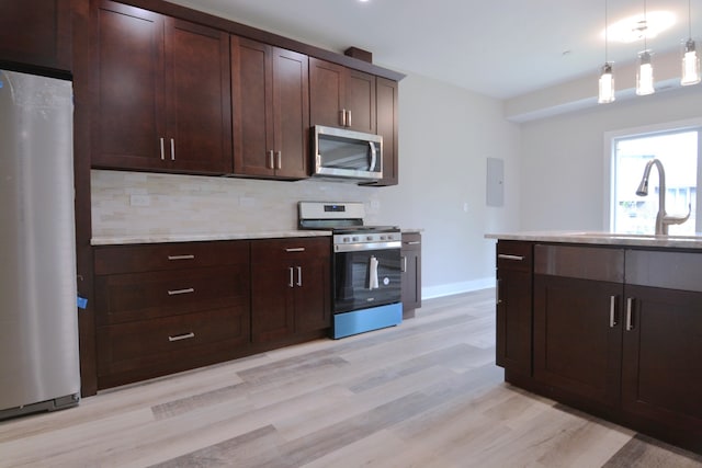 kitchen featuring hanging light fixtures, sink, backsplash, appliances with stainless steel finishes, and light hardwood / wood-style floors