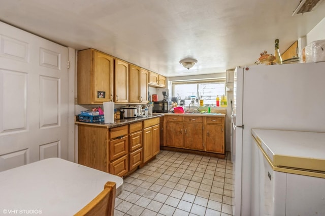 kitchen with brown cabinets, visible vents, light tile patterned floors, and freestanding refrigerator