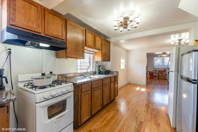 kitchen with white appliances, brown cabinets, under cabinet range hood, a sink, and a notable chandelier