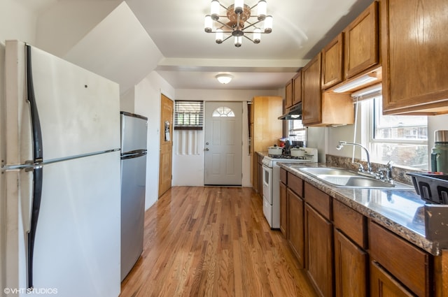 kitchen featuring sink, white appliances, light hardwood / wood-style flooring, an inviting chandelier, and dark stone counters