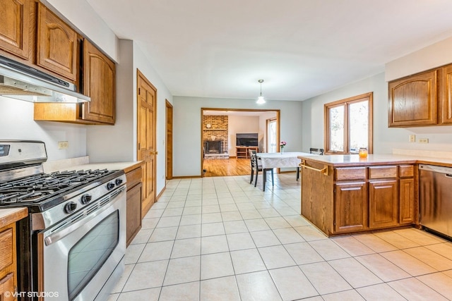 kitchen featuring appliances with stainless steel finishes, hanging light fixtures, kitchen peninsula, a brick fireplace, and light tile patterned floors