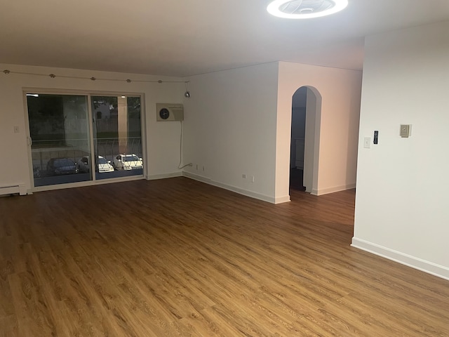 empty room featuring a baseboard radiator, a wall unit AC, and hardwood / wood-style flooring