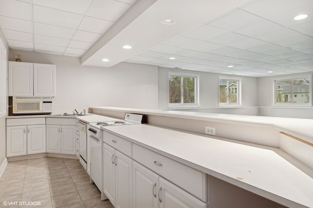 kitchen with a drop ceiling, white appliances, sink, light tile patterned floors, and white cabinetry