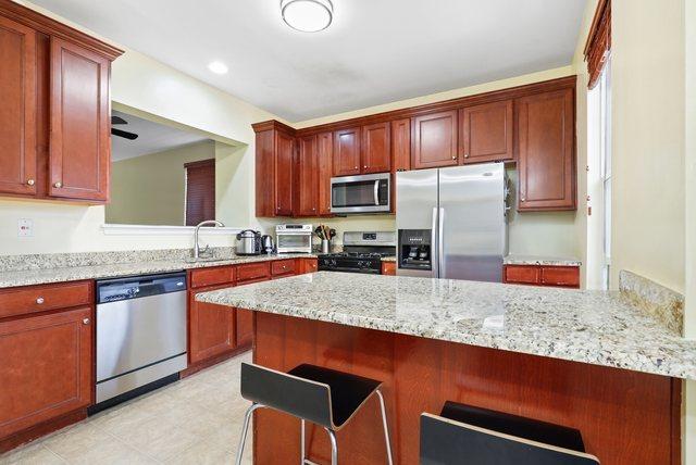 kitchen featuring light stone countertops, stainless steel appliances, ceiling fan, and a breakfast bar area