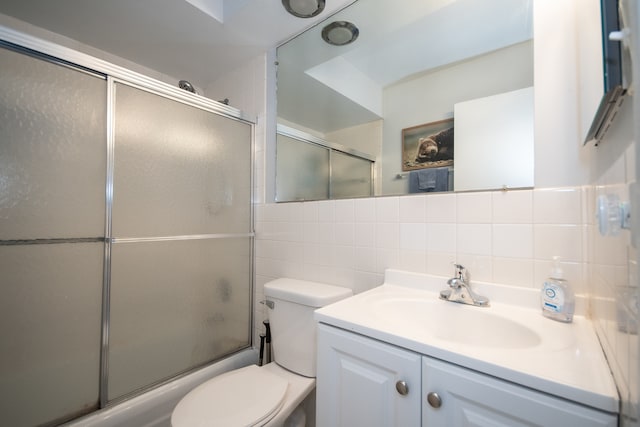 full bathroom featuring vanity, combined bath / shower with glass door, tile walls, toilet, and decorative backsplash