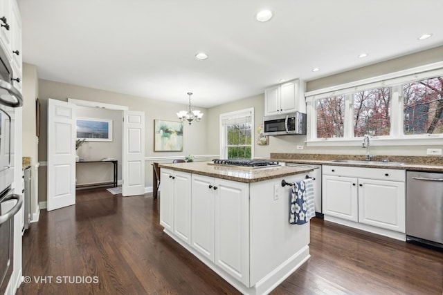 kitchen with decorative light fixtures, a center island, sink, stainless steel appliances, and white cabinets