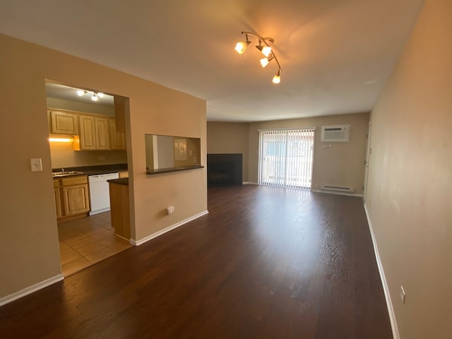 unfurnished living room with an AC wall unit, dark hardwood / wood-style floors, a baseboard heating unit, and sink