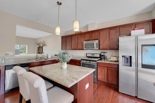 kitchen featuring light stone counters, stainless steel appliances, light hardwood / wood-style flooring, decorative light fixtures, and sink