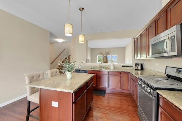 kitchen with sink, kitchen peninsula, stainless steel appliances, a kitchen breakfast bar, and hardwood / wood-style floors