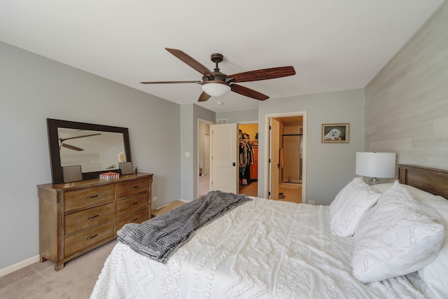 bedroom with ceiling fan, a walk in closet, a closet, light carpet, and ensuite bath