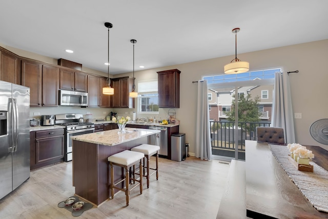 kitchen with dark brown cabinetry, pendant lighting, stainless steel appliances, a center island, and light hardwood / wood-style floors