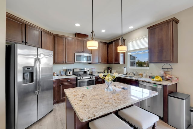 kitchen with appliances with stainless steel finishes, light hardwood / wood-style floors, light stone countertops, pendant lighting, and a center island