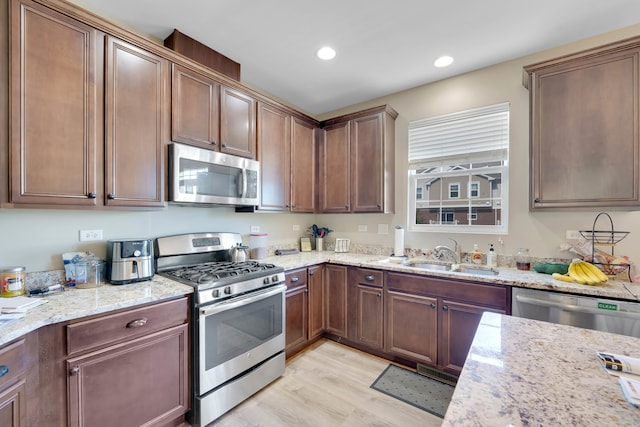 kitchen featuring stainless steel appliances, light stone counters, light wood-type flooring, and sink